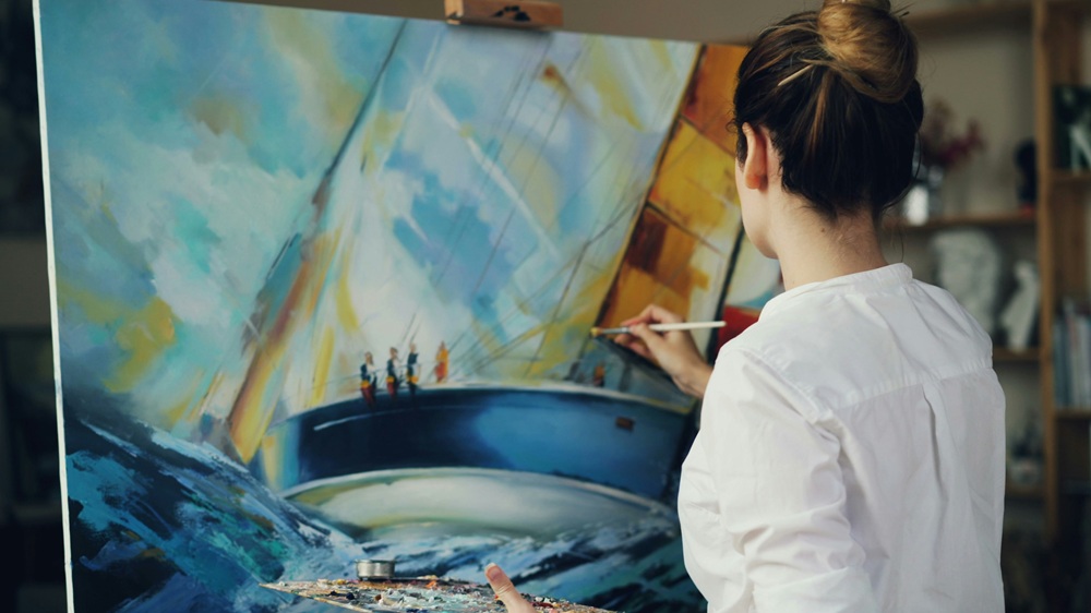 Mujer pintando un cuadro de un velero, expresando creatividad y bienestar