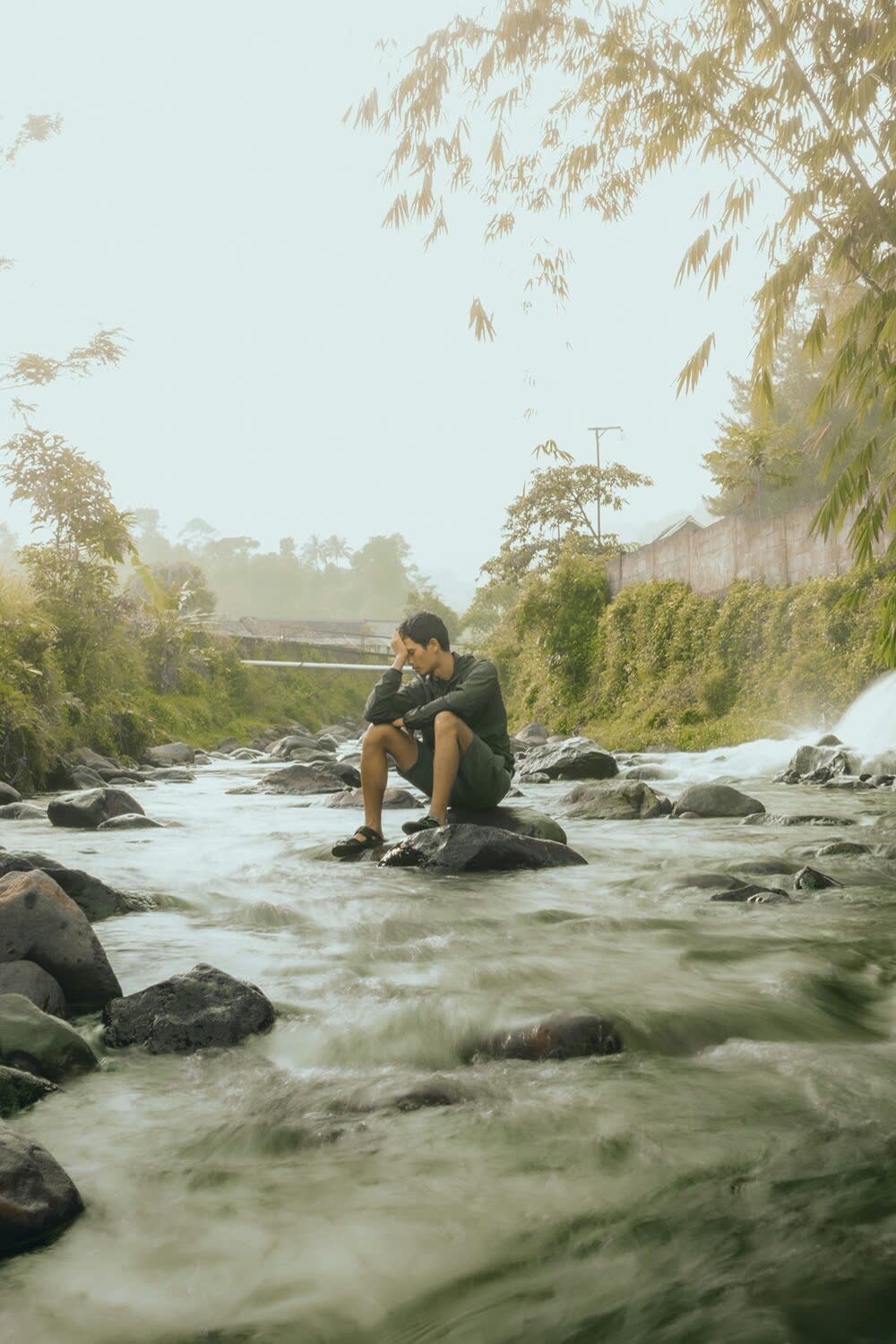 Hombre reflexivo sentado junto a un río representando baja autoestima